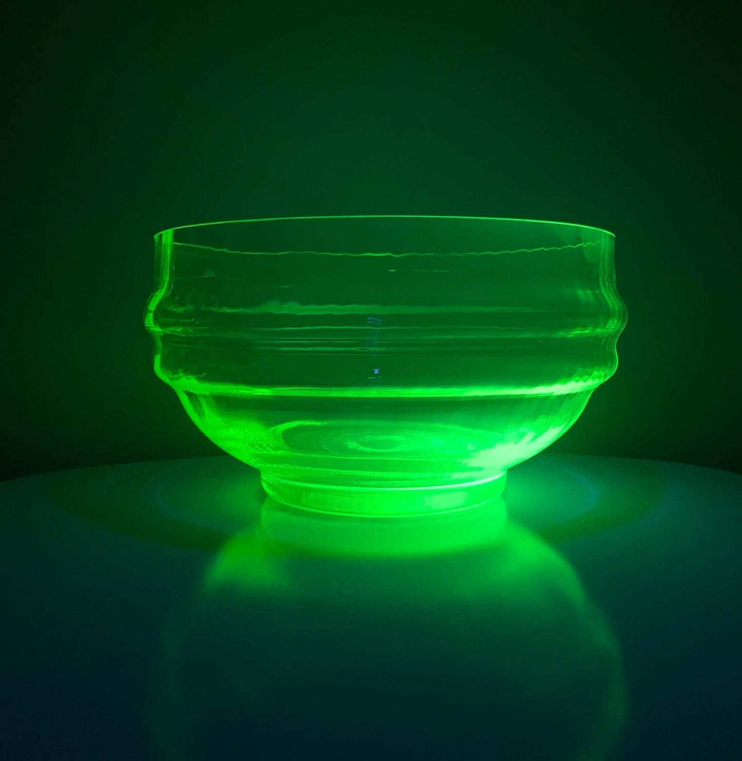 UV Glowing green glass bowl on a reflective surface with a dark background